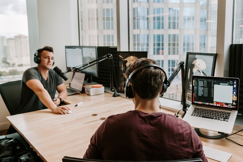 two men sitting by the table using microphone and headphones inside studio during daytime