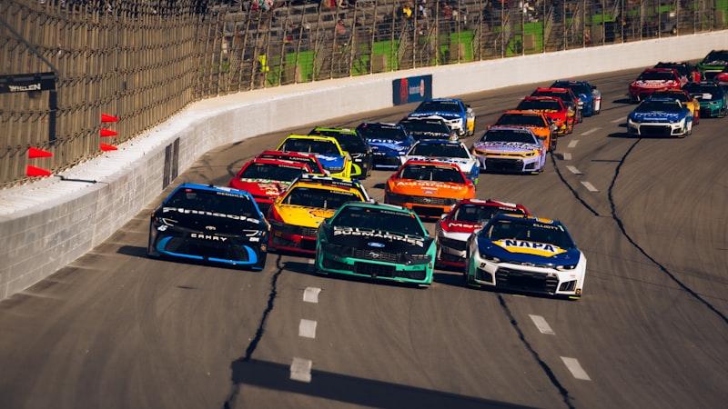 Stock cars race closely on a paved track.