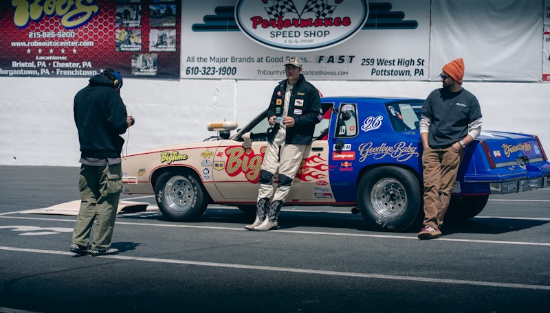 Three people stand by a race car on a track.