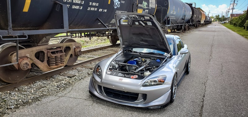 A car with open hood next to a train.